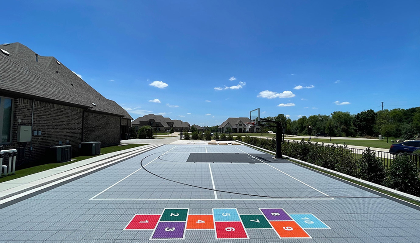 An outdoor multi‑sport court with a basketball hoop and a colorful hopscotch grid
