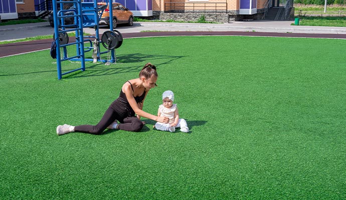 A woman sitting with her baby on soft green artificial turf in a garden